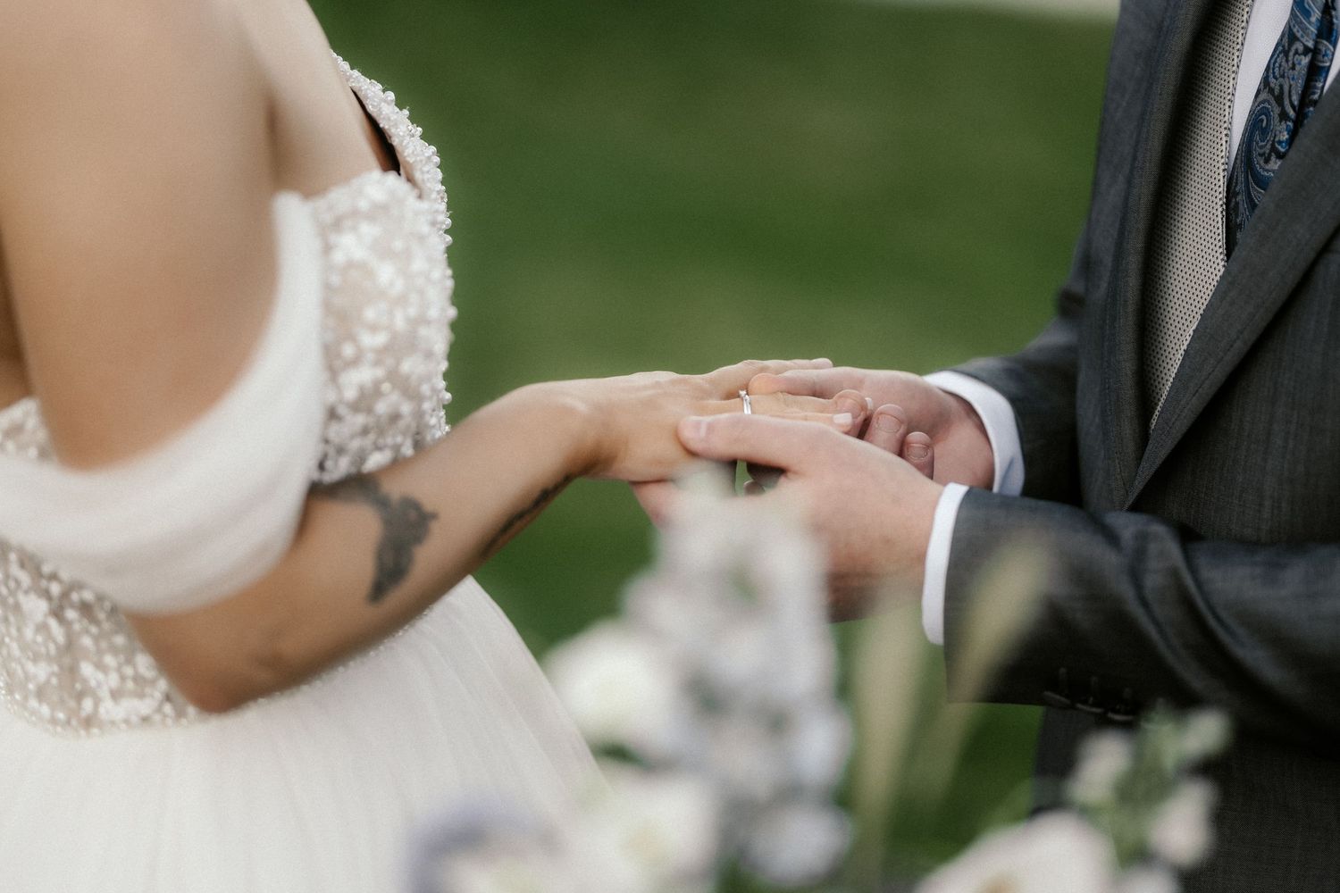 Close-up of hands exchanging rings during an outdoor wedding ceremony.