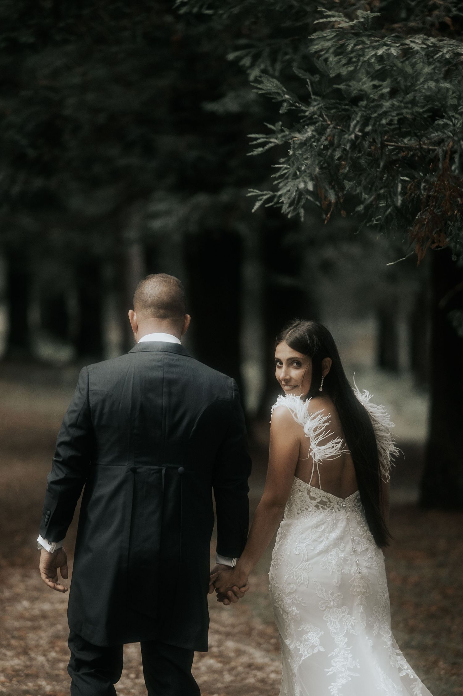 A wedding couple walks through a wooded path, with the bride's white dress flowing elegantly.