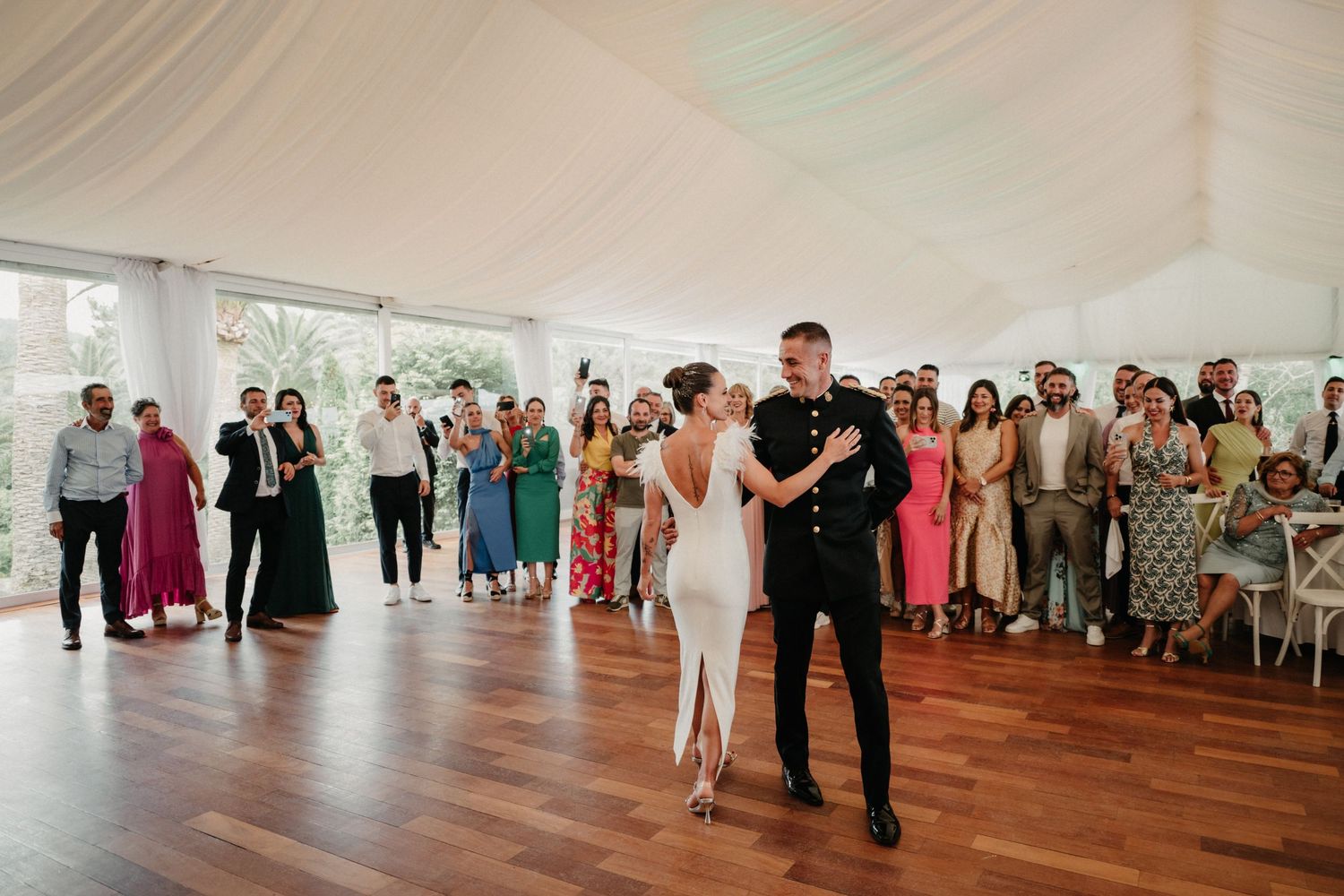 Wedding guests dance together on a wooden floor under a white tent during a reception celebration.