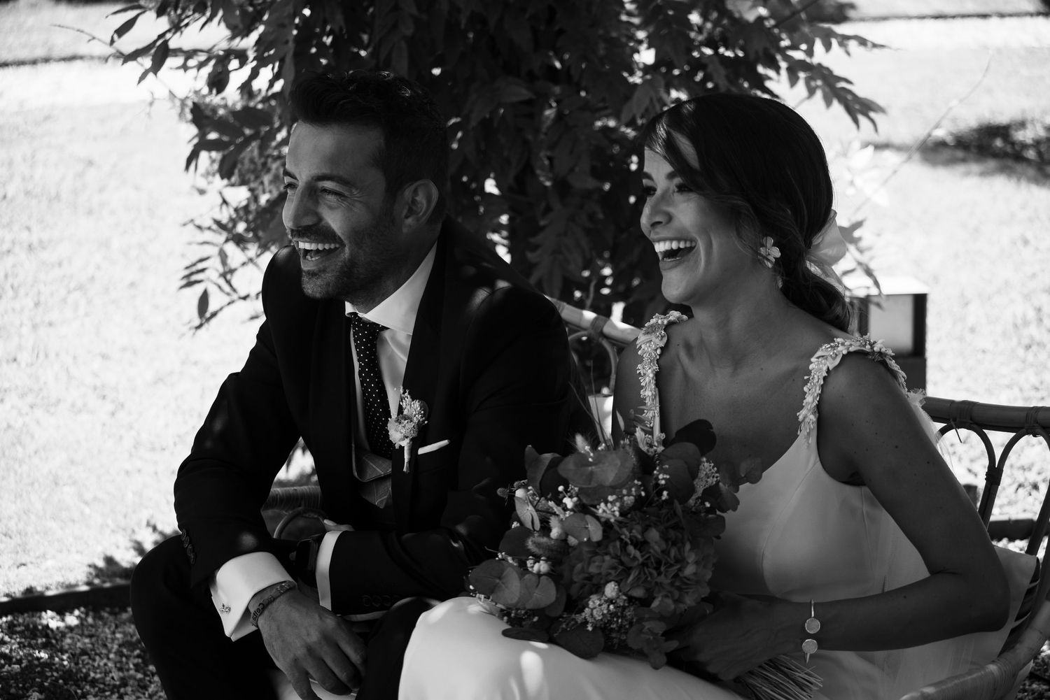 Joyful wedding couple sharing a candid laughing moment together outdoors.