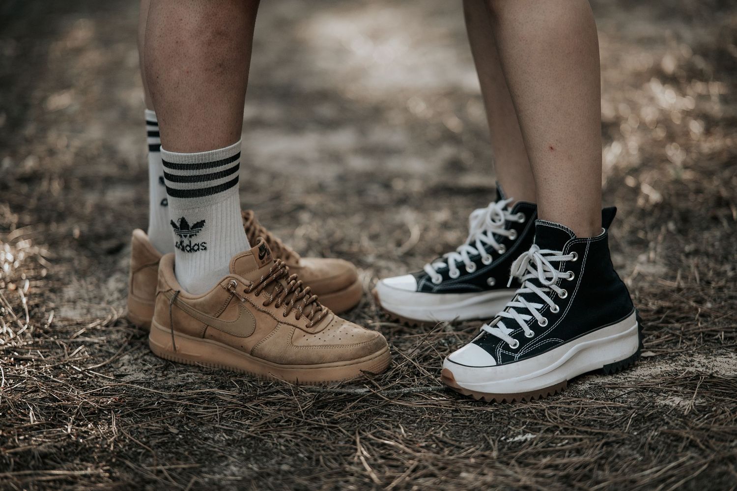 A series of feet wearing different styles of shoes standing on natural ground.