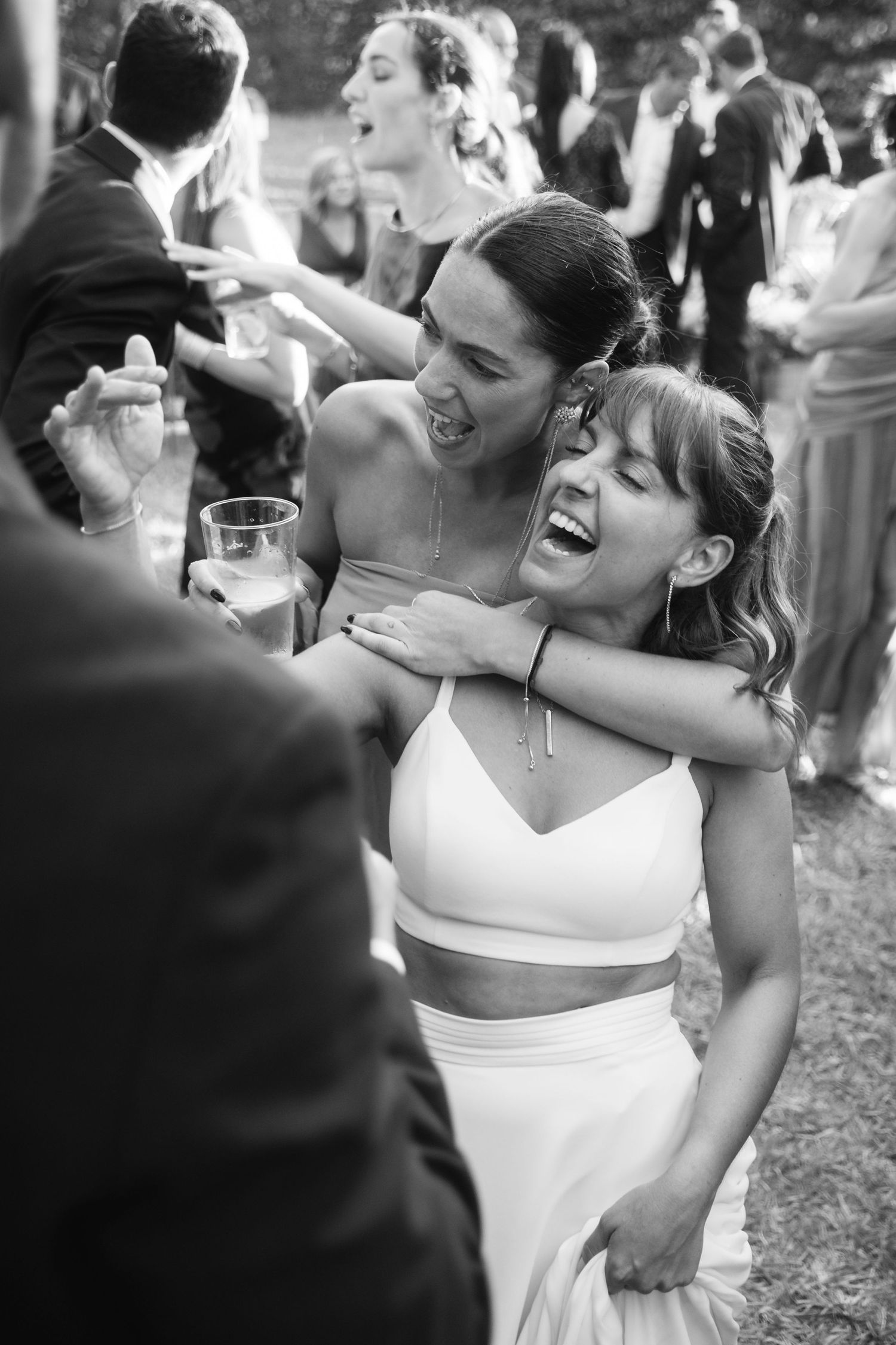 Candid black and white photo of wedding guests laughing and dancing during a reception celebration.