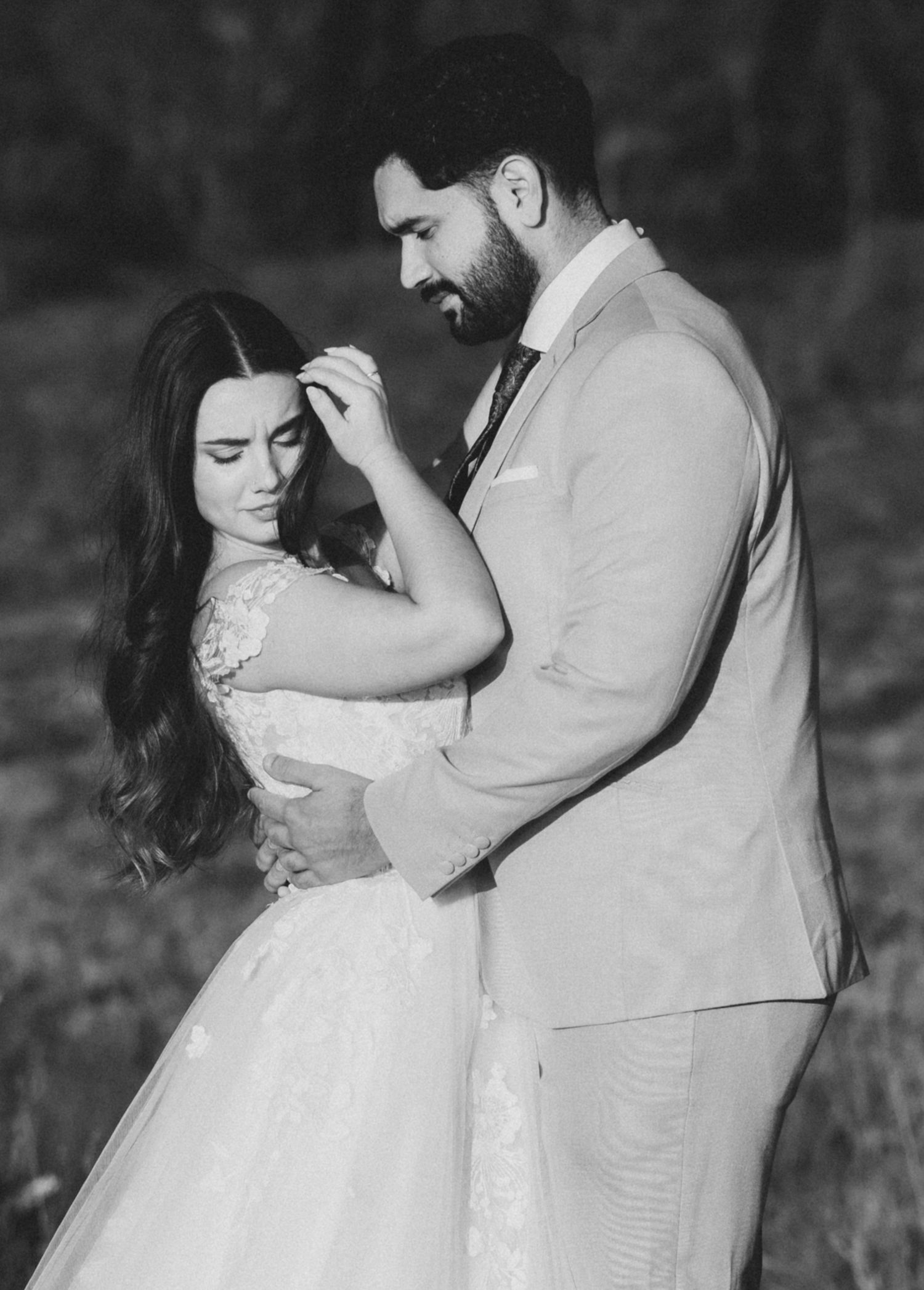 A romantic black and white wedding portrait of a couple embracing, with the bride wearing a lace dress.