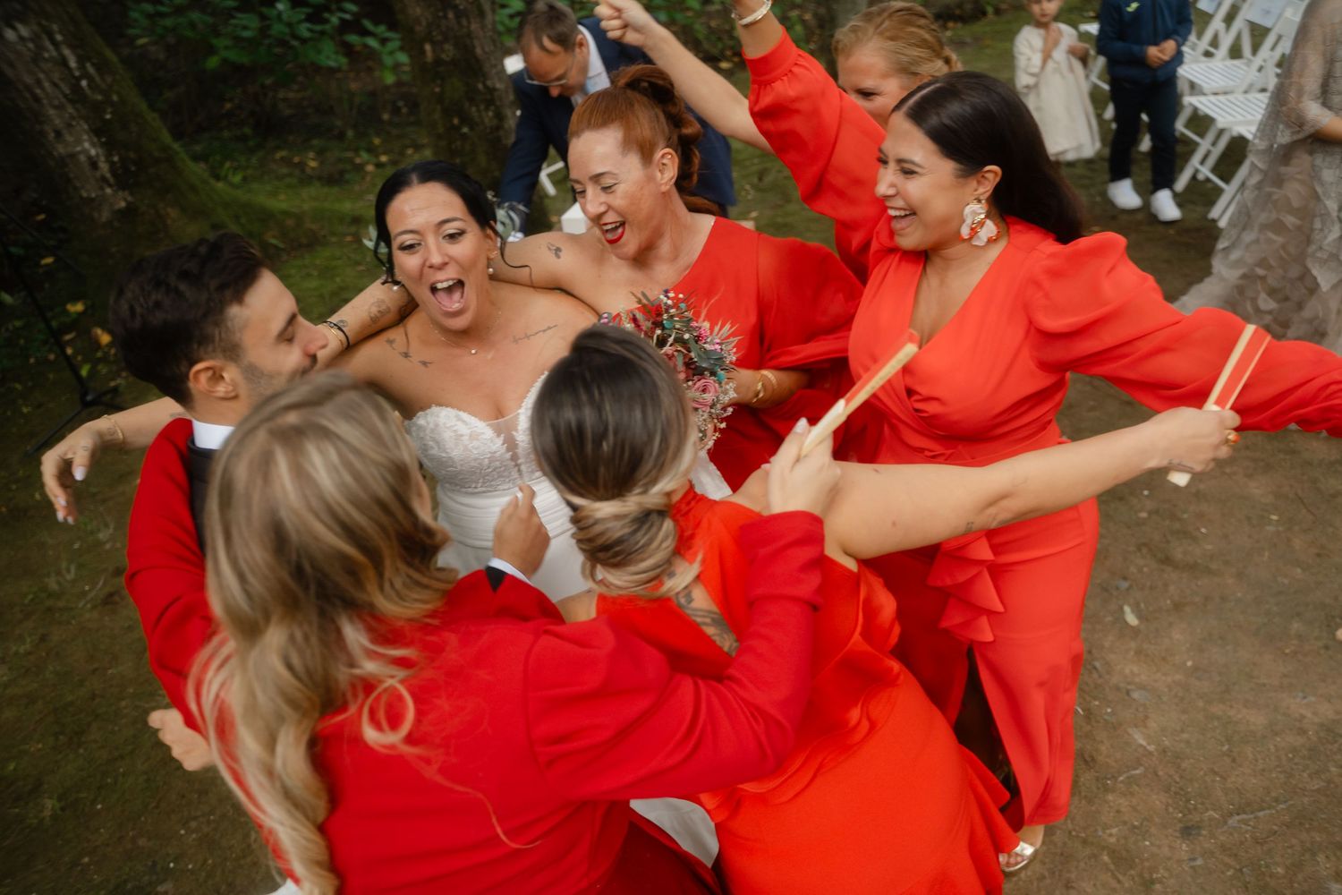 Wedding party in bright red attire celebrates joyfully during outdoor reception.