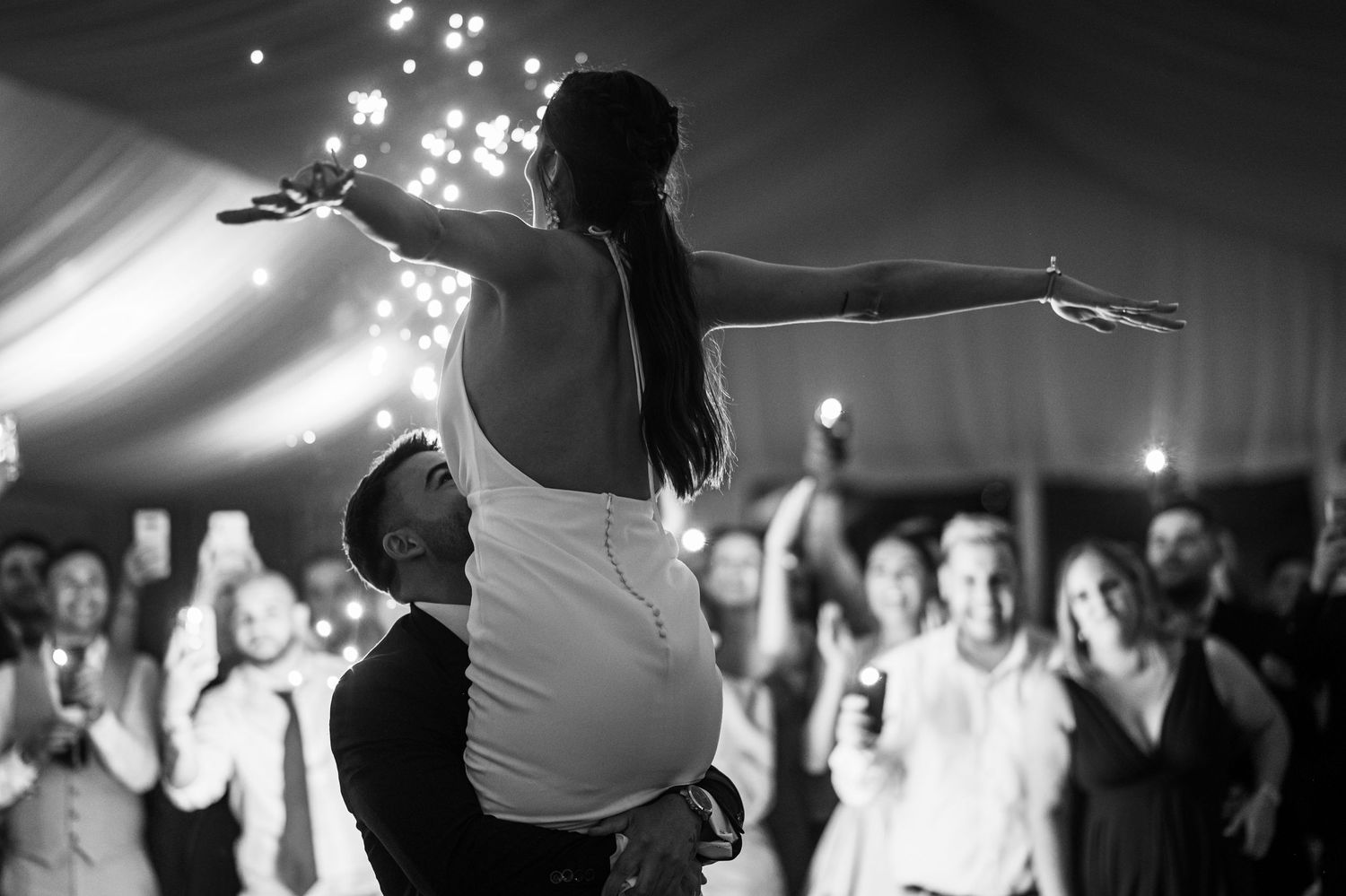 Black and white photo of couples dancing together at a lively party with twinkling lights in the background.