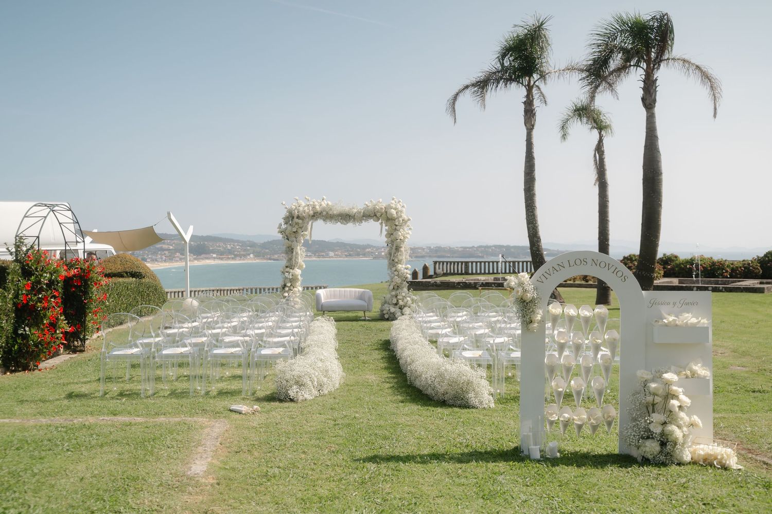 Elegant outdoor wedding ceremony setup with white chairs and palm trees by the ocean.