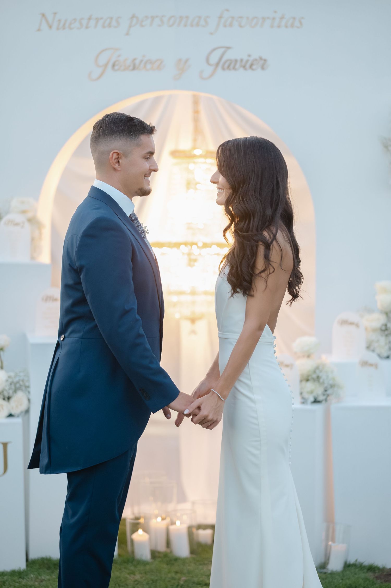 A romantic wedding couple poses together under an elegant white archway with soft lighting.