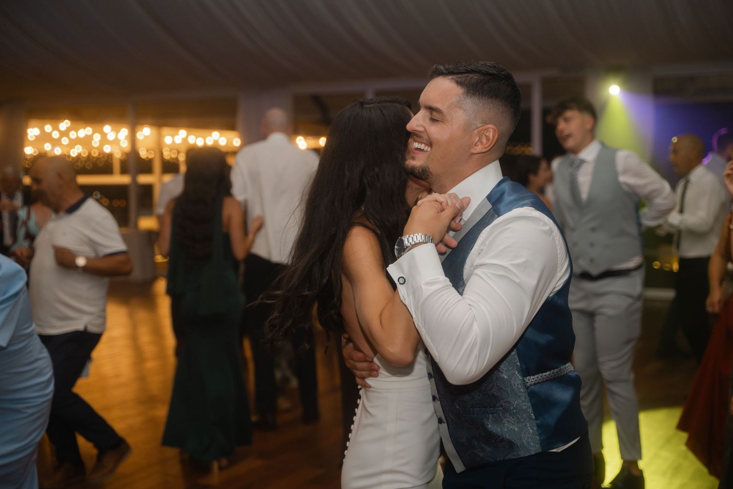 People dancing and celebrating at a wedding reception with warm lighting and festive atmosphere.
