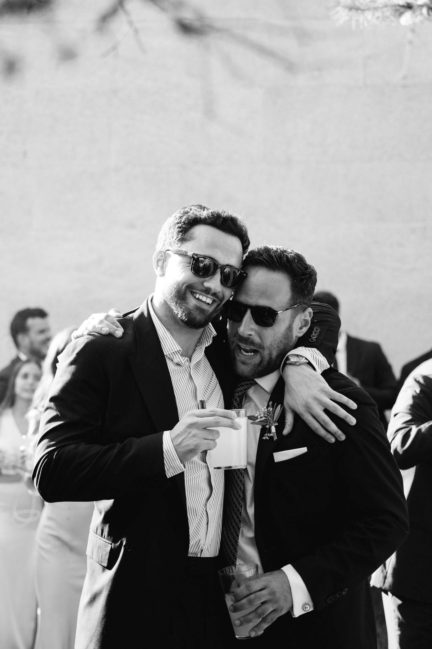 Groomsmen in suits laughing and embracing at an outdoor wedding celebration.