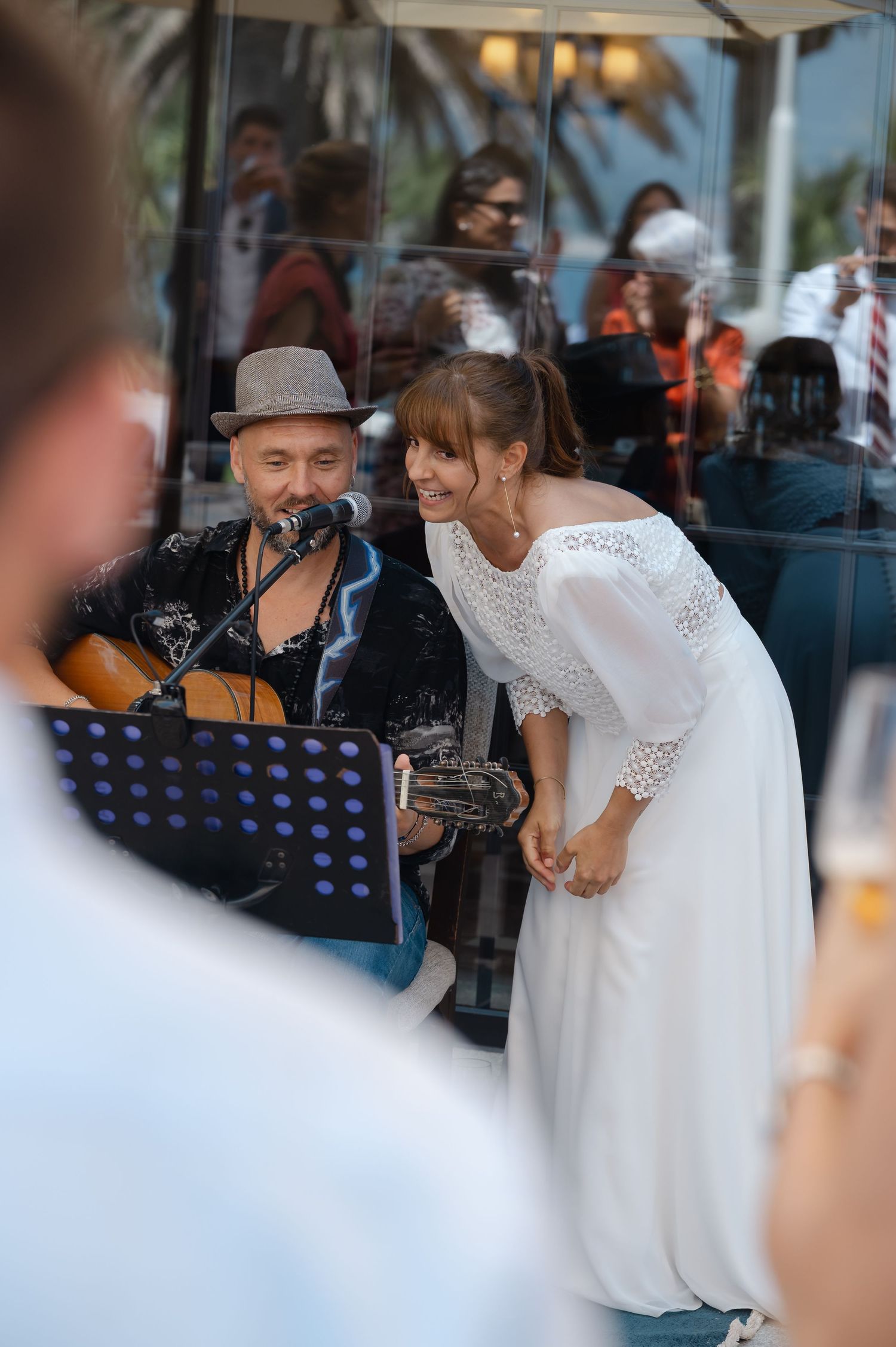 A bride in a white lace dress interacts with musicians during what appears to be a wedding celebration.