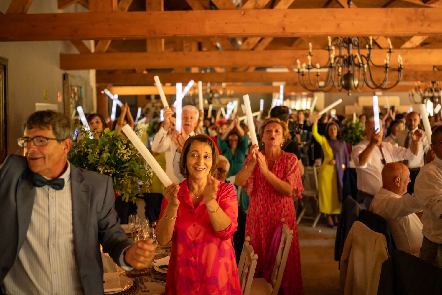 Wedding reception guests dance and celebrate under warm lighting in a rustic wooden venue.