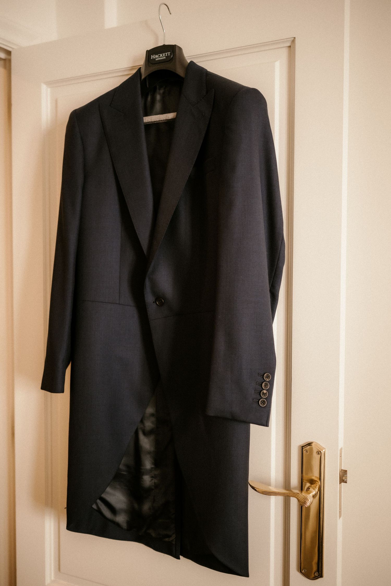A black formal suit jacket hanging on a white door with brass hardware.