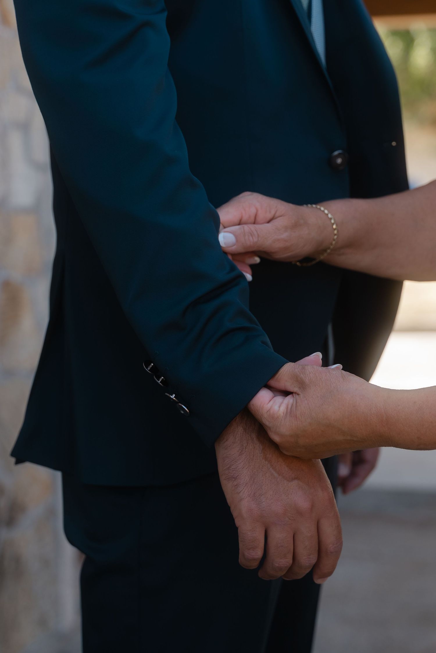 Close-up view of hands clasped together wearing formal dark attire in natural lighting.