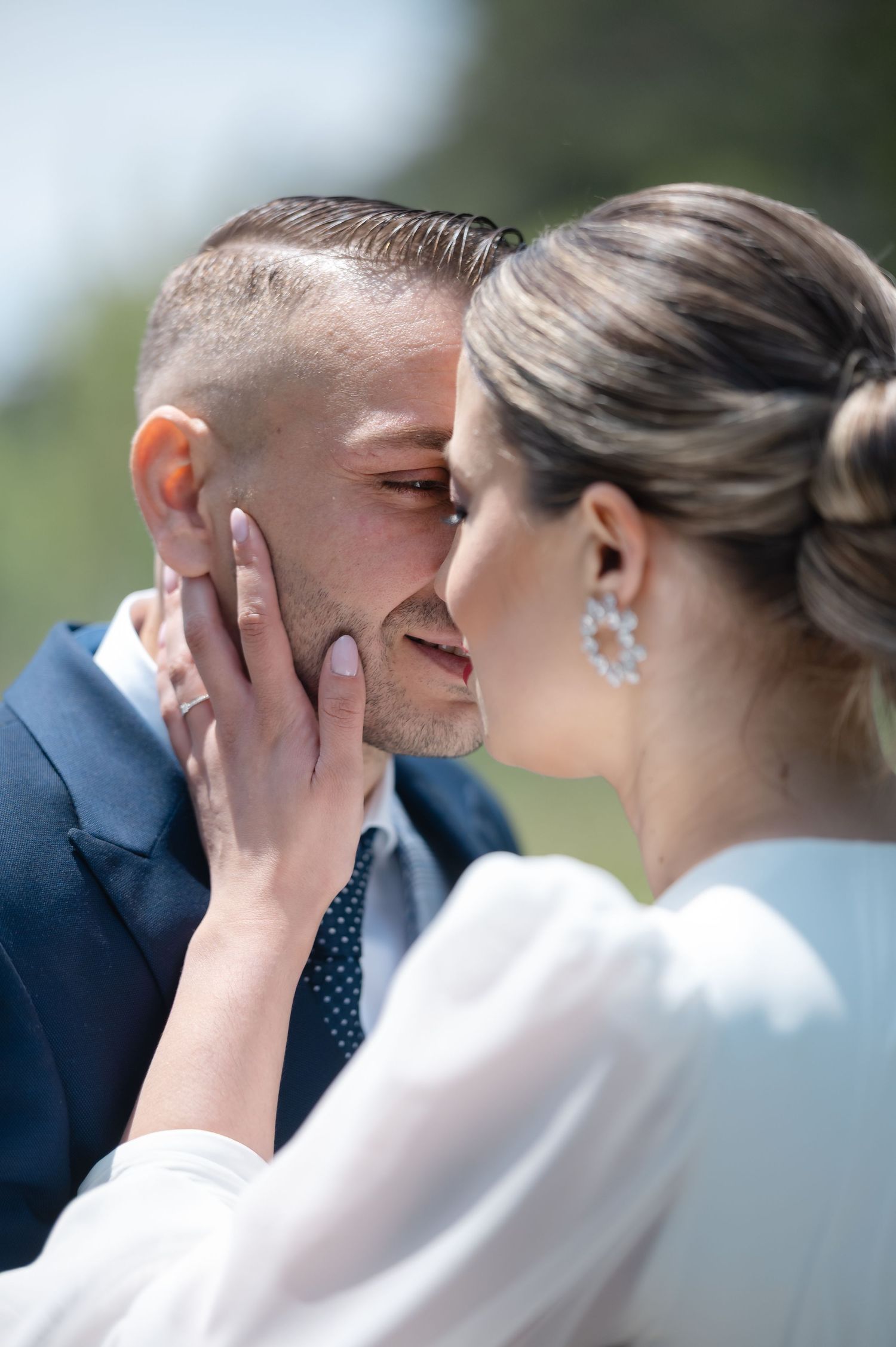 A couple in wedding attire share an intimate kiss outdoors during their special day.