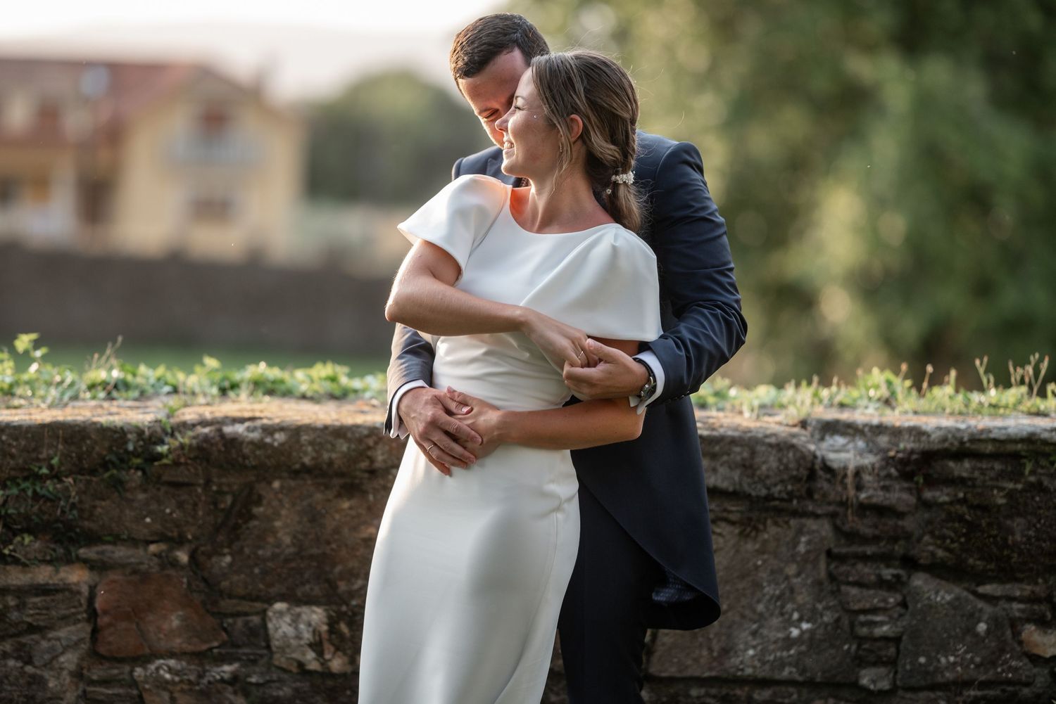 A couple embraces tenderly against a stone wall during a romantic outdoor wedding photo session.