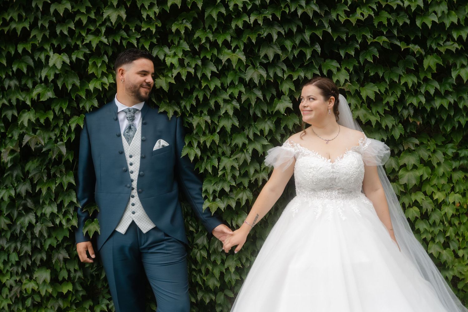 A couple shares a joyful moment together against a lush ivy wall backdrop during their wedding celebration.