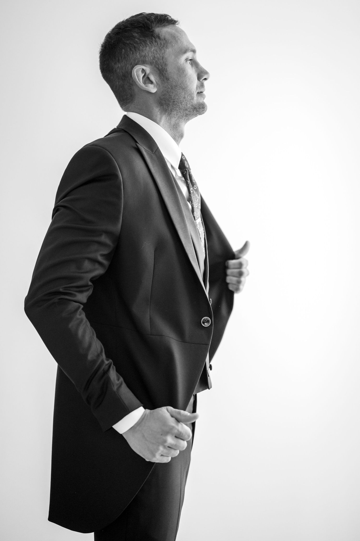 Professional black and white portrait series showing a man in suit jacket posing against white background.