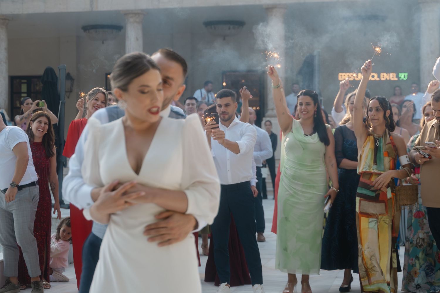 Wedding guests watch a couple's first dance in a room filled with atmospheric smoke.