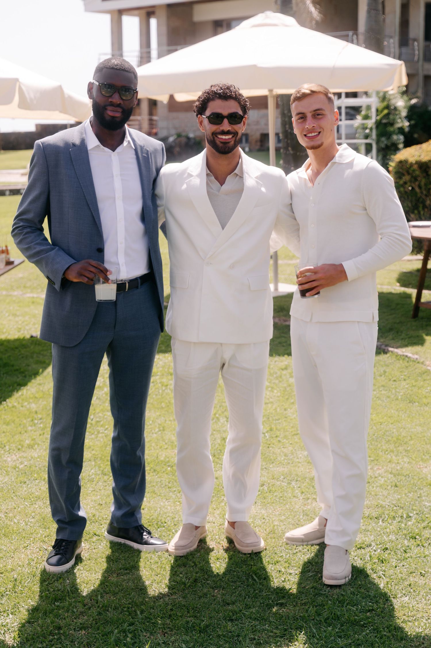 A wedding party poses on green grass wearing white suits and a navy suit, creating a stylish contrast outdoors.