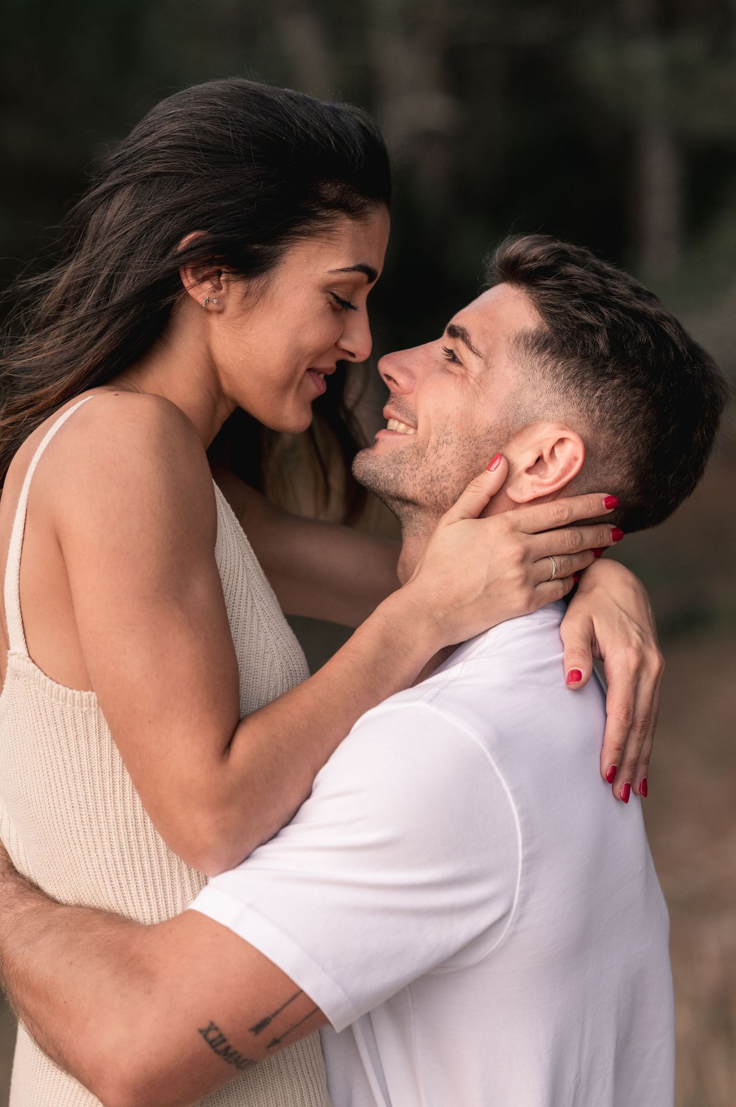 An intimate moment captured between a couple wearing white and beige against a blurred natural backdrop.