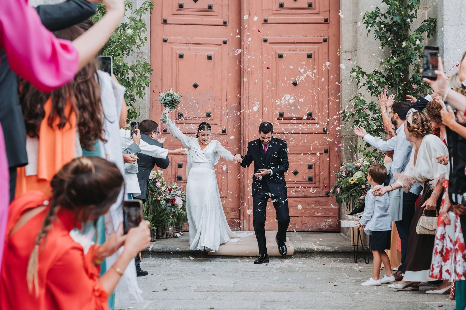 Wedding celebration outside pink church doors with guests throwing flower petals.