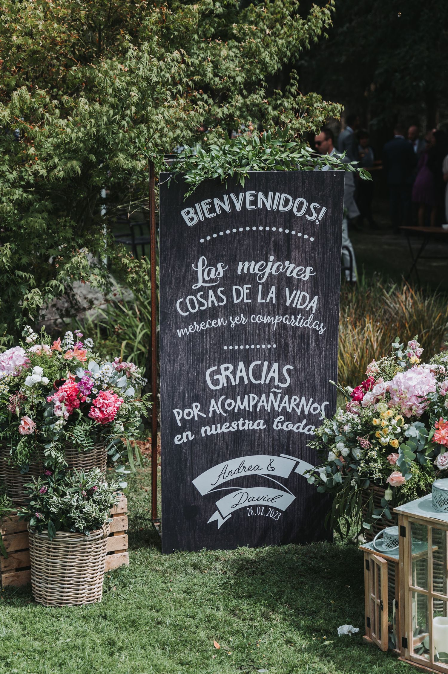 Rustic chalkboard wedding signs with Spanish text decorated with floral arrangements and wooden crates in an outdoor garden setting.