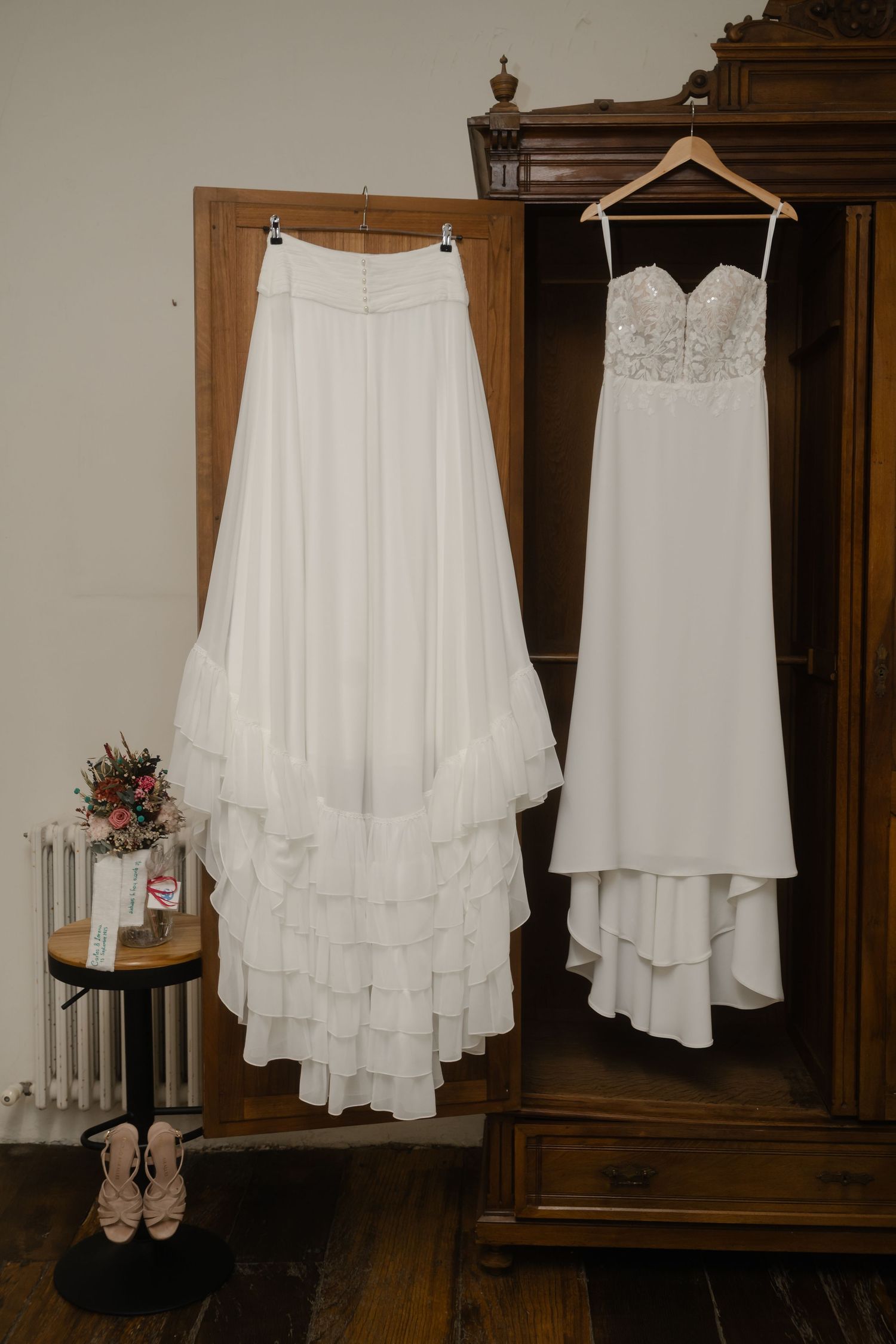 White wedding dresses and shoes displayed on hangers against a wooden wardrobe.