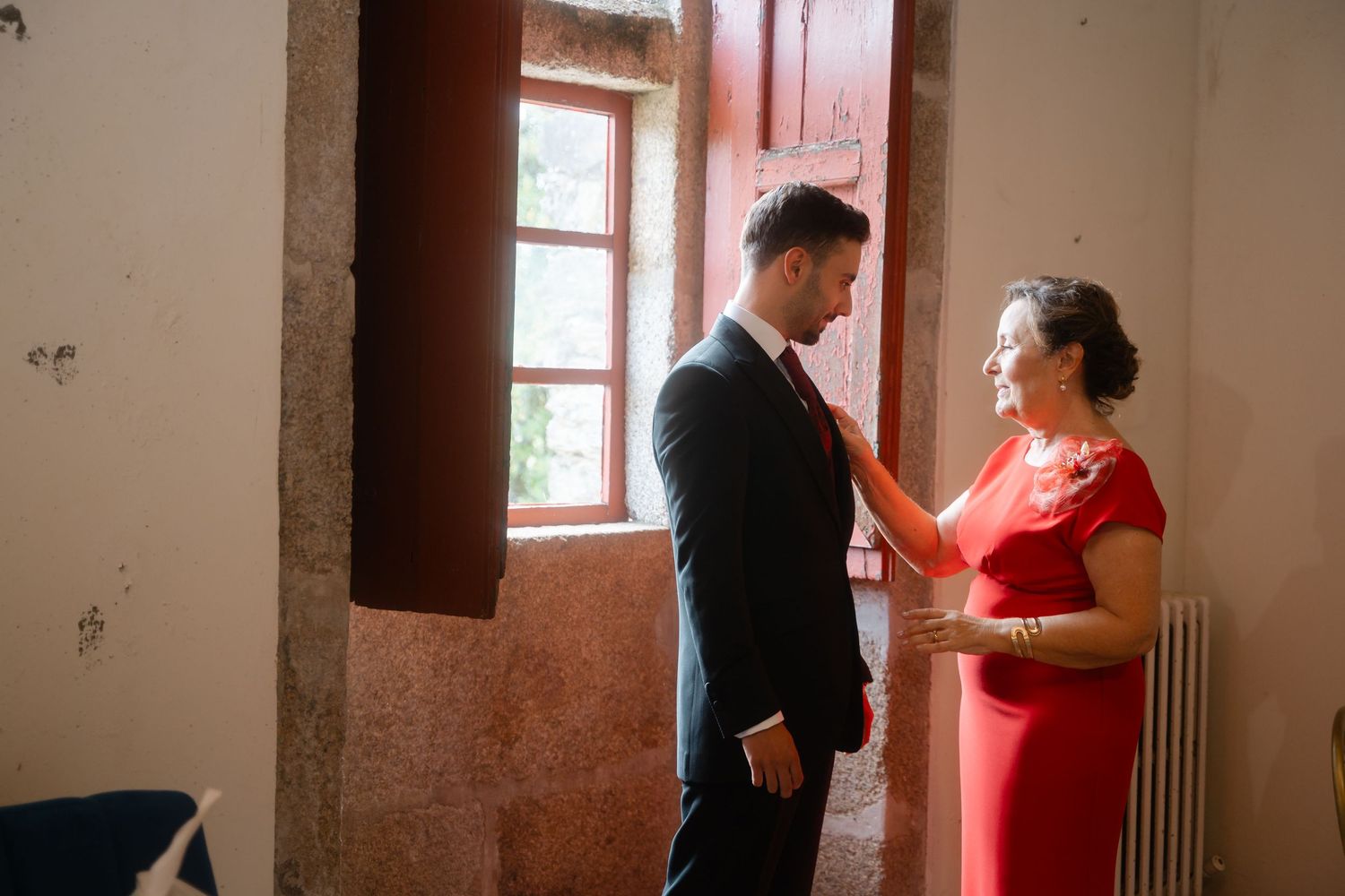 A touching pre-event scene shows two people sharing an intimate moment near a window in a red-walled room.