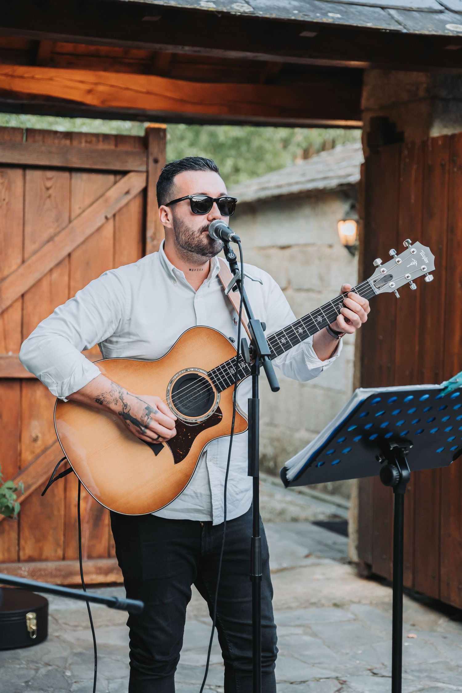 Musician performs with acoustic guitar at rustic wooden venue wearing dark pants and light colored shirt.
