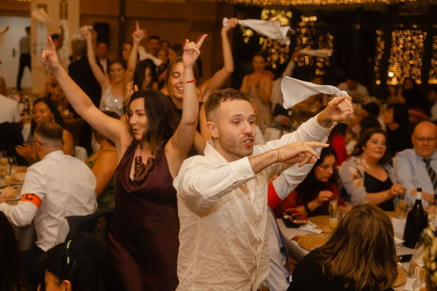 Wedding guests dancing and celebrating with raised arms on a crowded dance floor.