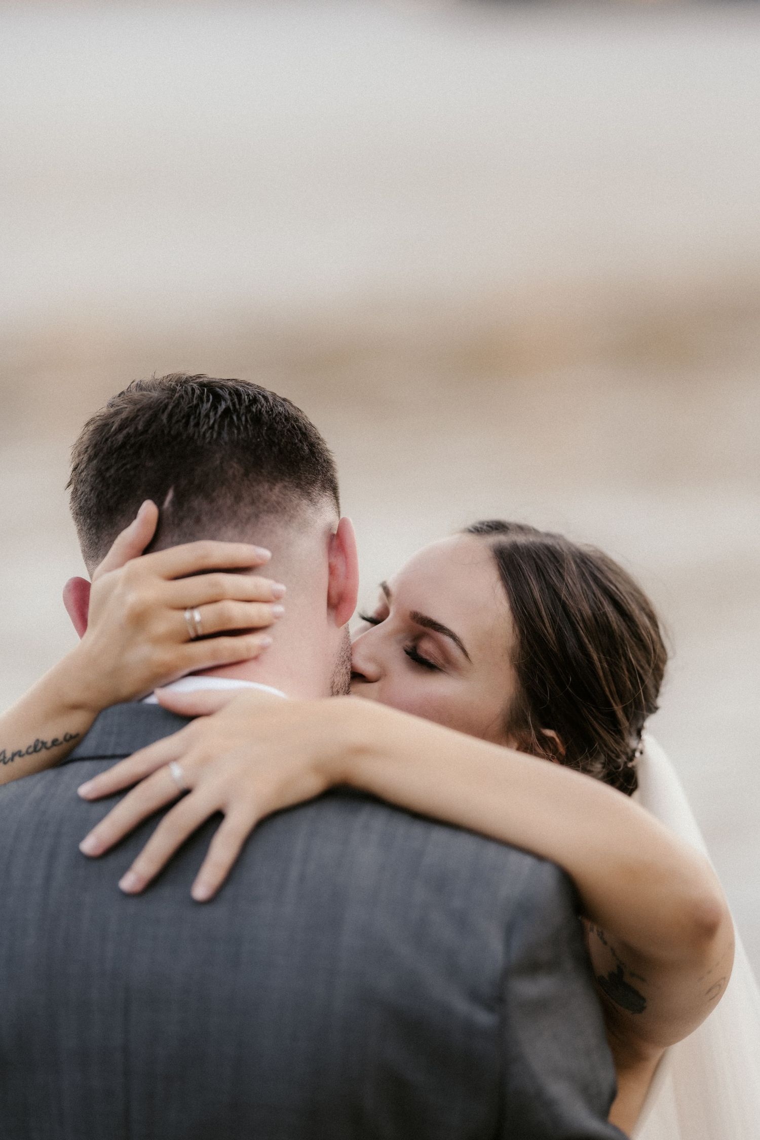 Close-up series of intimate wedding couple embracing in gray suit and white dress against soft background.