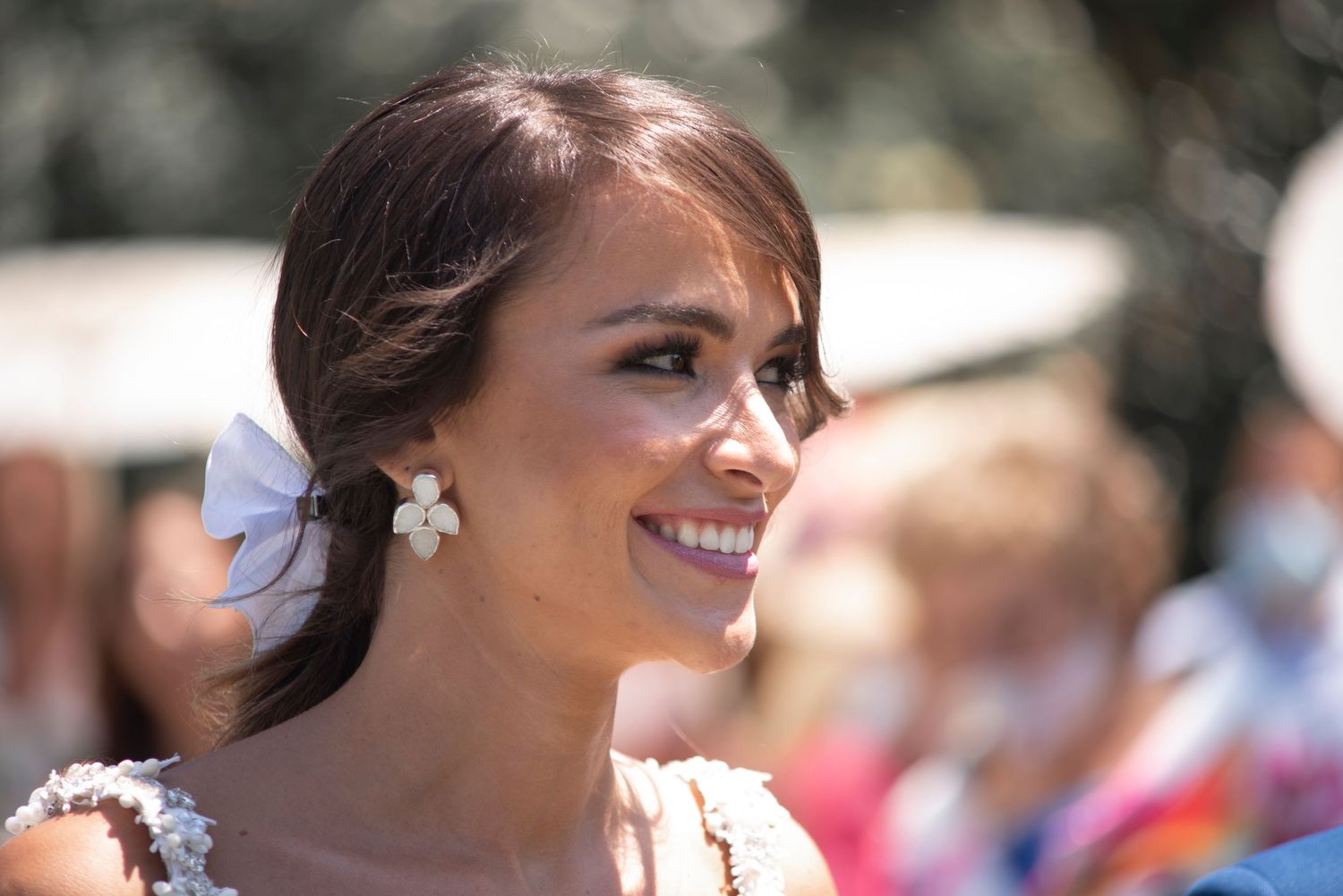A bride in a white wedding dress smiles outdoors with a delicate floral hair accessory.