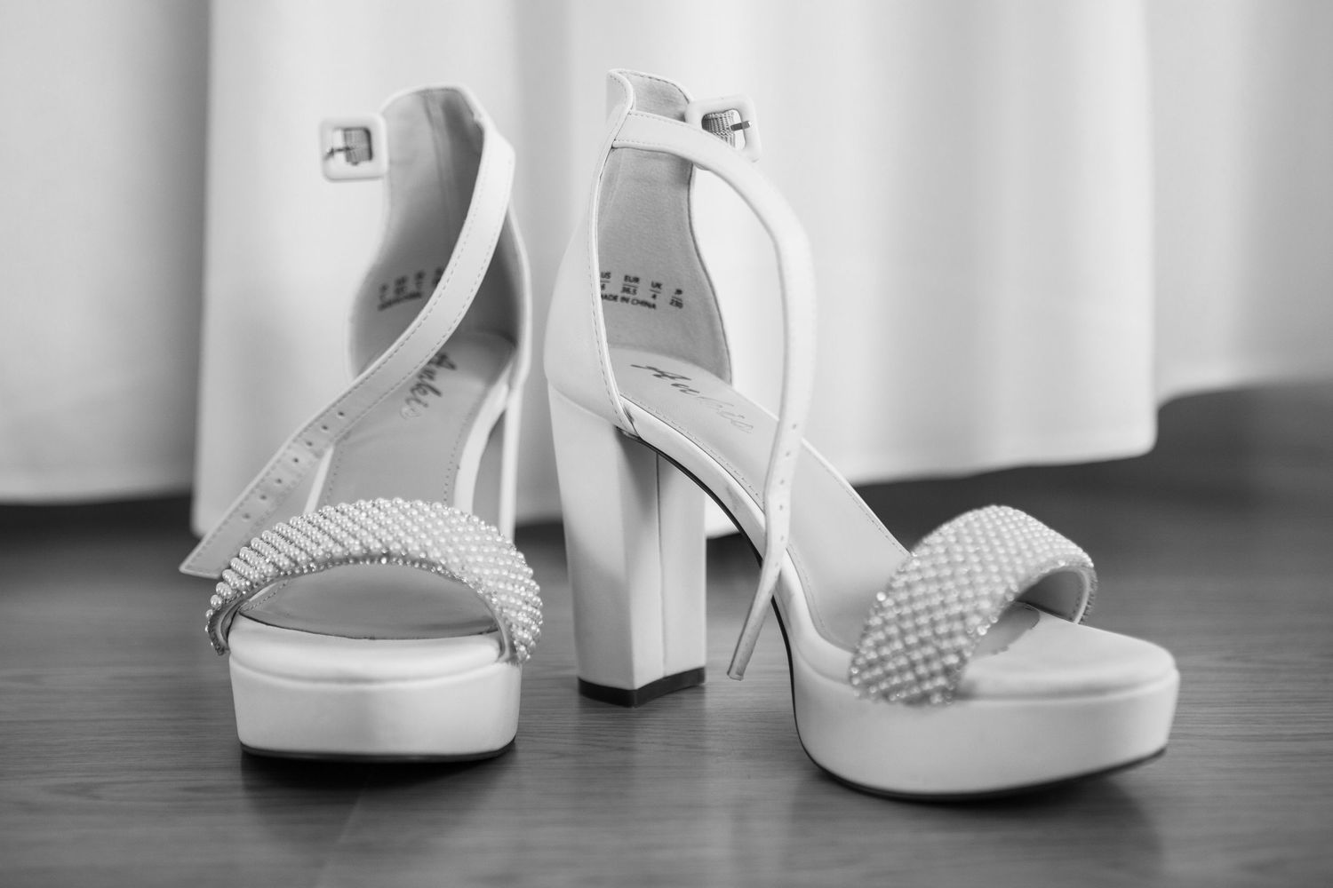 A pair of elegant white platform high heels with braided straps photographed in black and white.