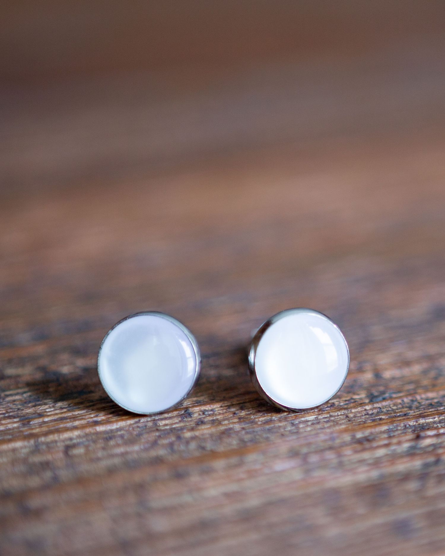 Simple white pearl stud earrings shown in a sequence of close-up shots on a rustic wooden surface.