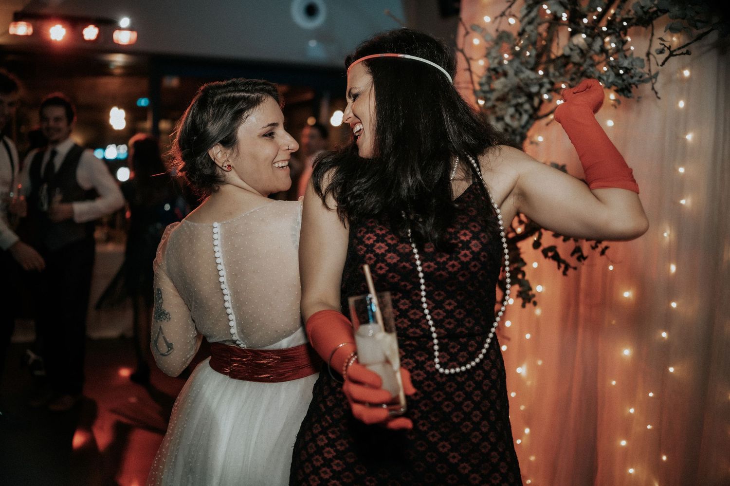 Couples dancing together at a dimly lit wedding reception with warm red lighting and string lights in the background.