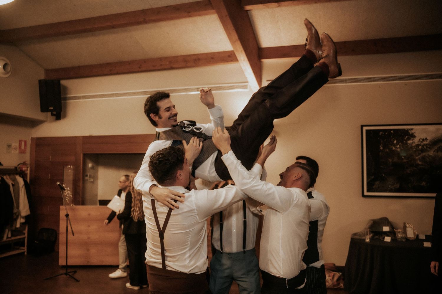 People dancing and celebrating at a wedding reception in a rustic venue with warm lighting.