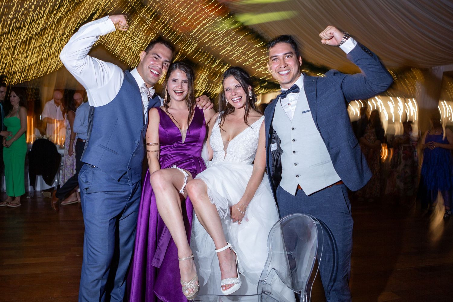 Wedding party celebrates on dance floor with purple bridesmaid dresses under string lights.