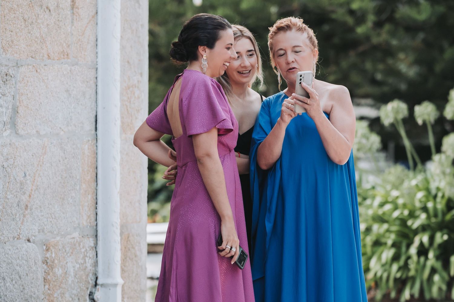 Wedding party members in purple and blue dresses share emotional reactions during outdoor celebration.