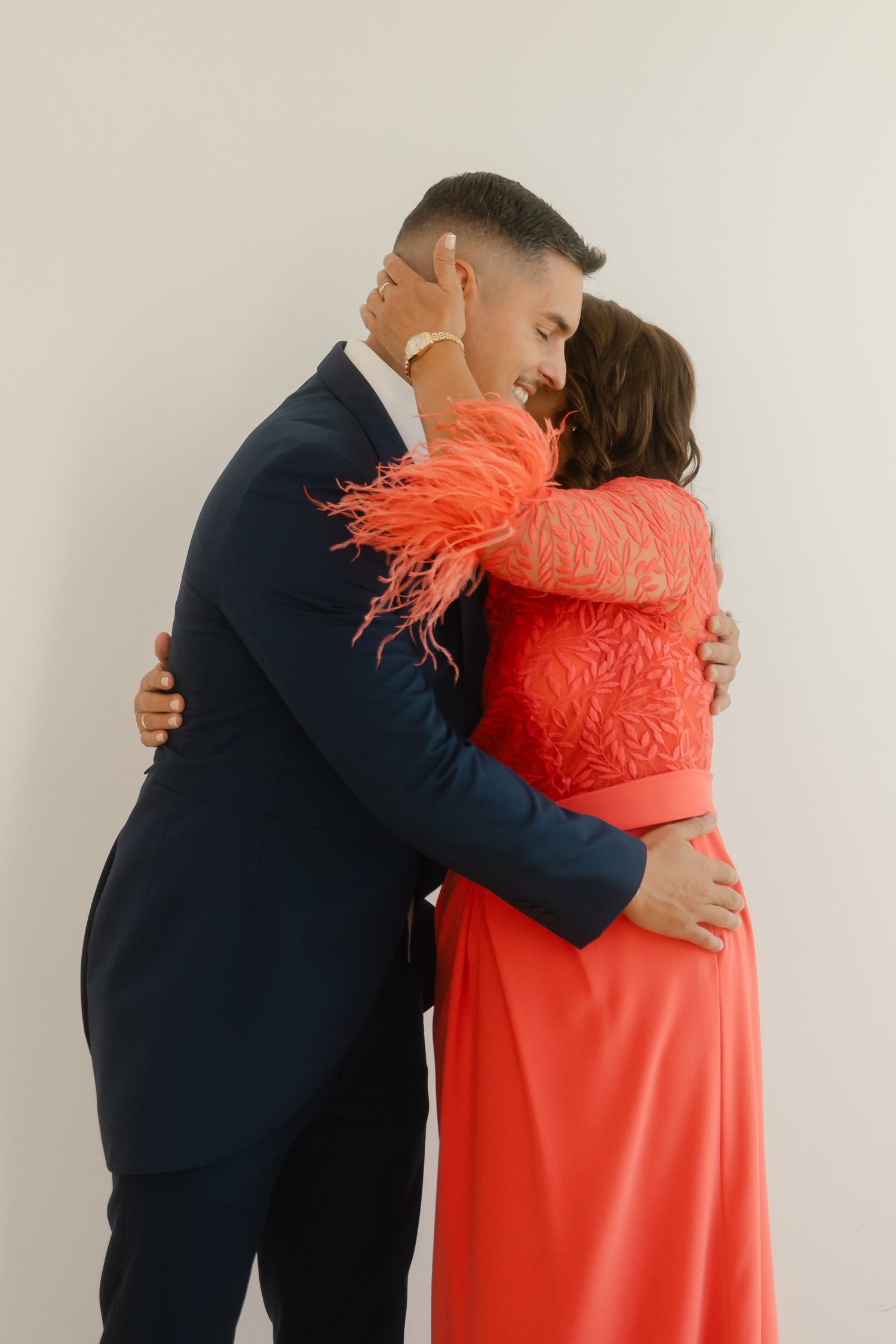 A couple embraces in a series of four photos, with one person wearing navy and the other in a coral dress with feather details.