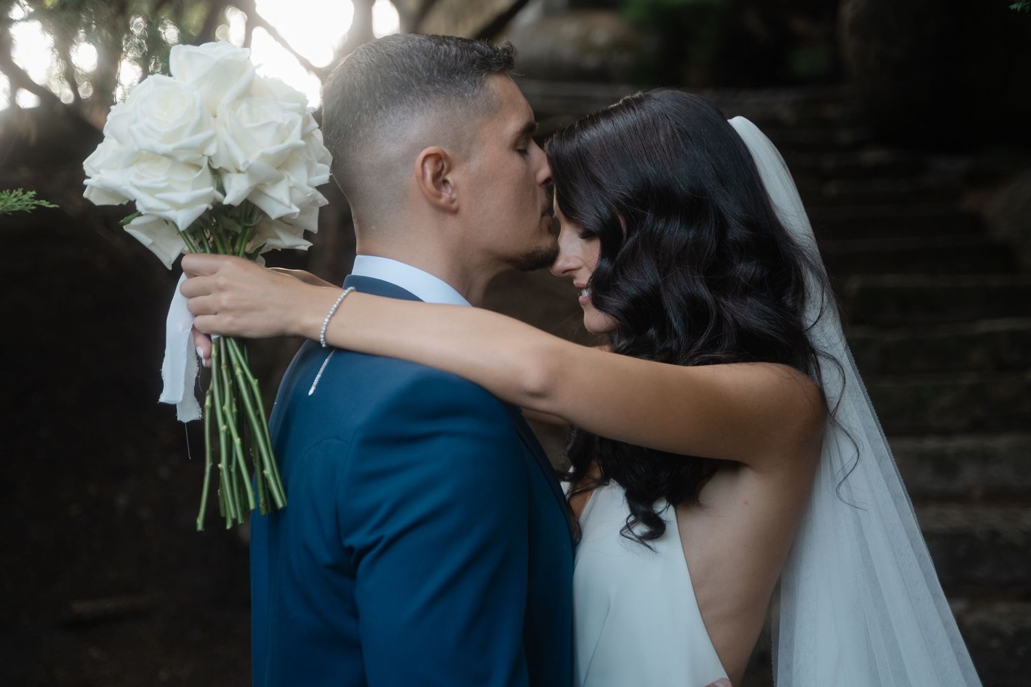 A bride and groom share an intimate moment during their wedding photoshoot in a rustic outdoor setting.