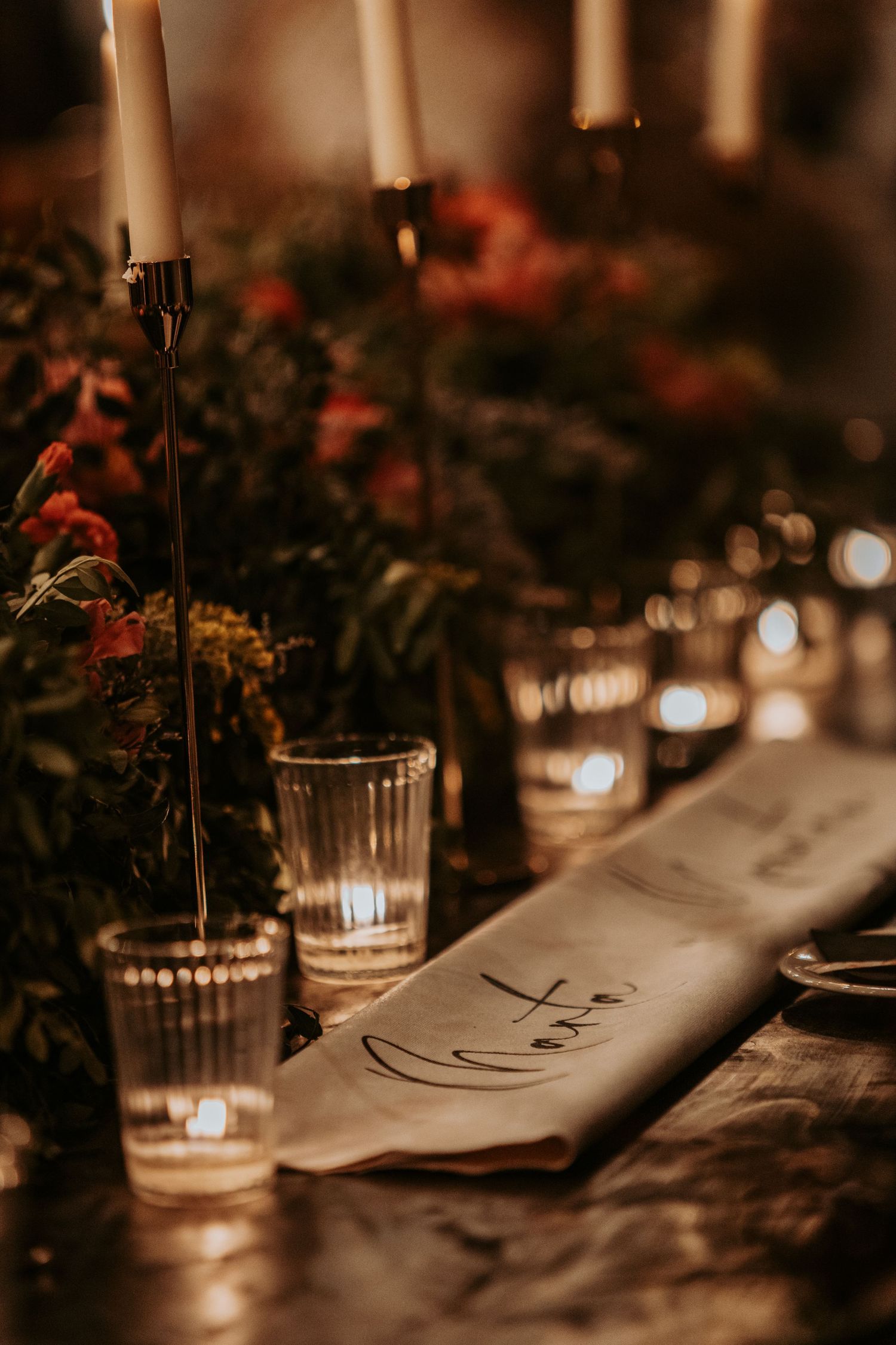 Elegant table setting at a wedding reception with candlelight and dark moody ambiance.