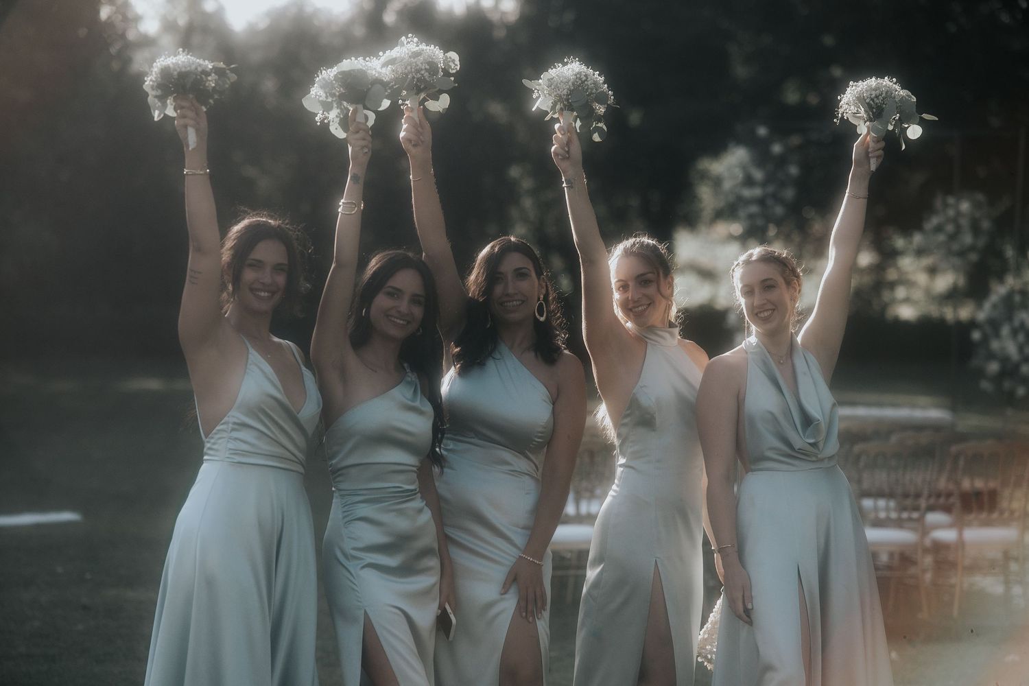 Bridesmaids in light blue dresses celebrate together during outdoor wedding celebration.