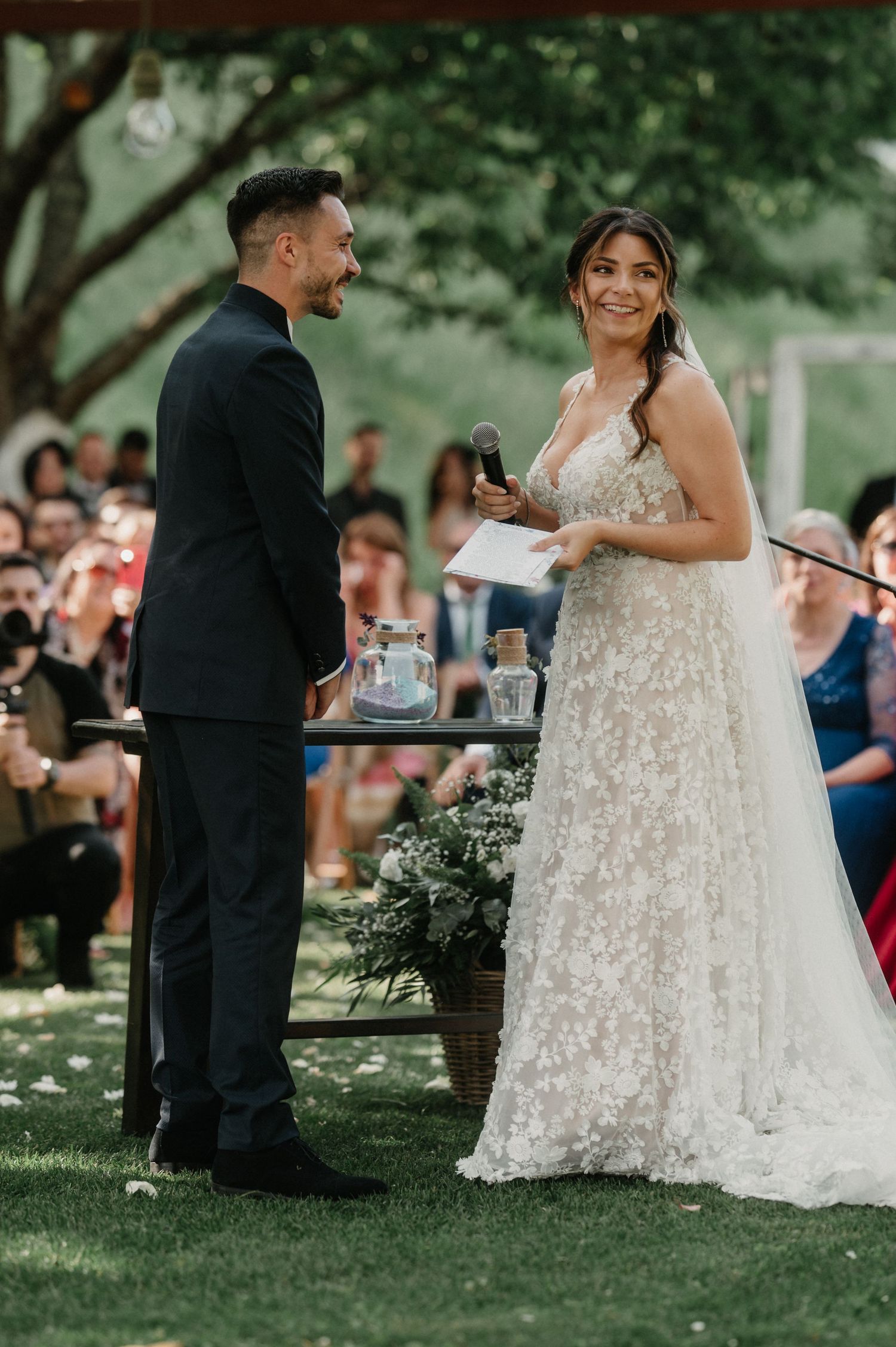 Wedding couple participates in a unity ceremony outdoors surrounded by guests on a sunny day.