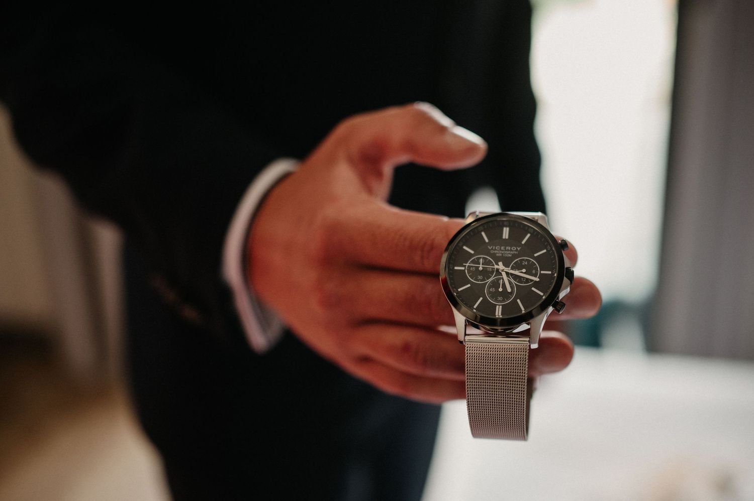 Close-up view of hands adjusting a luxury wristwatch with black dial and stainless steel bracelet.