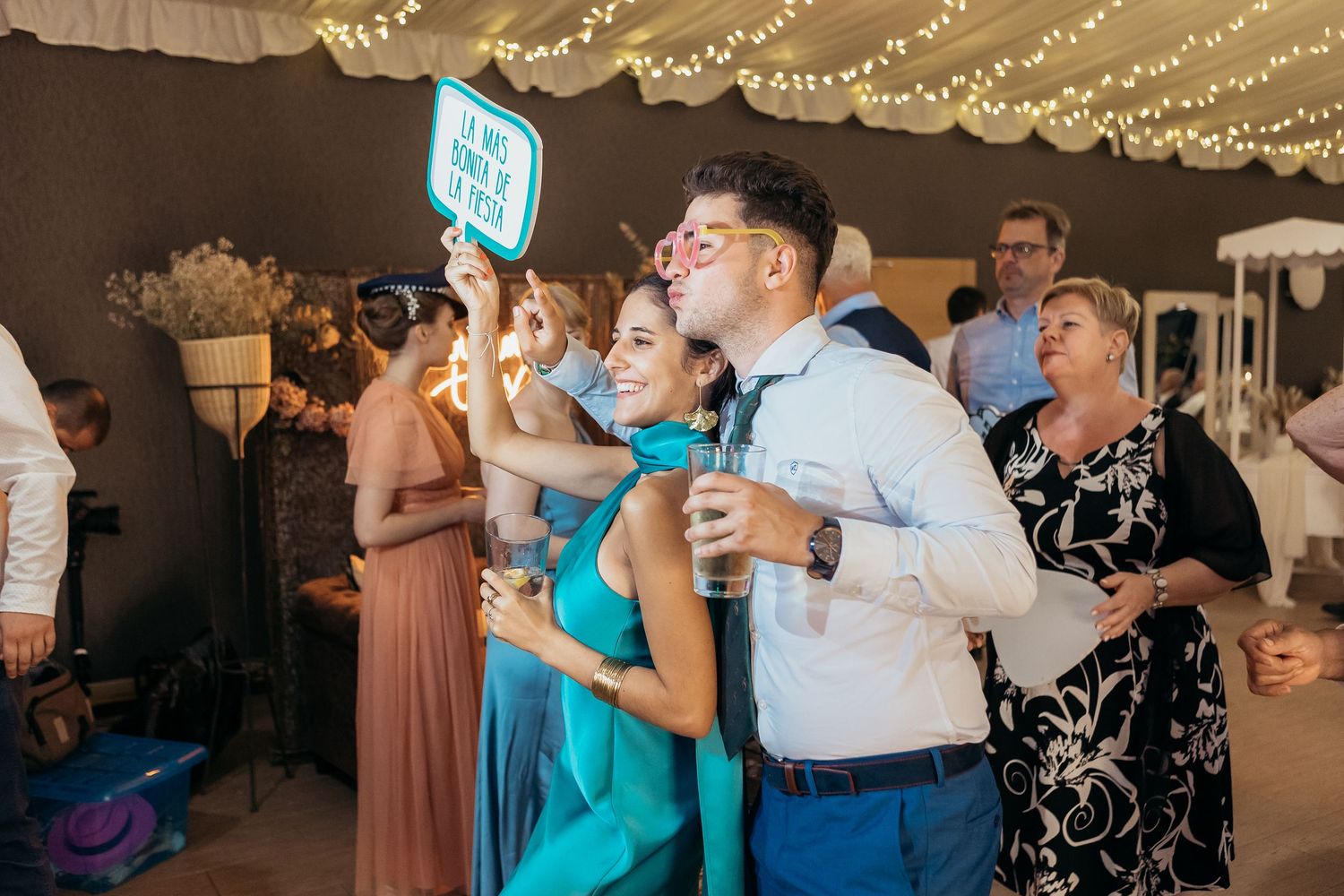 Wedding reception venue decorated with string lights as guests dance and celebrate under warm lighting.