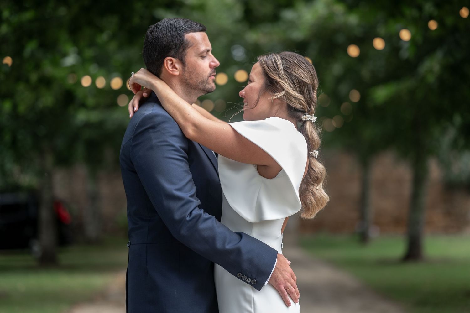 Newlywed couple shares an intimate dance moment outdoors with string lights twinkling in the background.