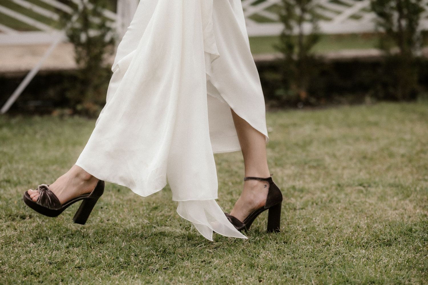 Series of elegant white wedding dress and black heels details on a grassy lawn.