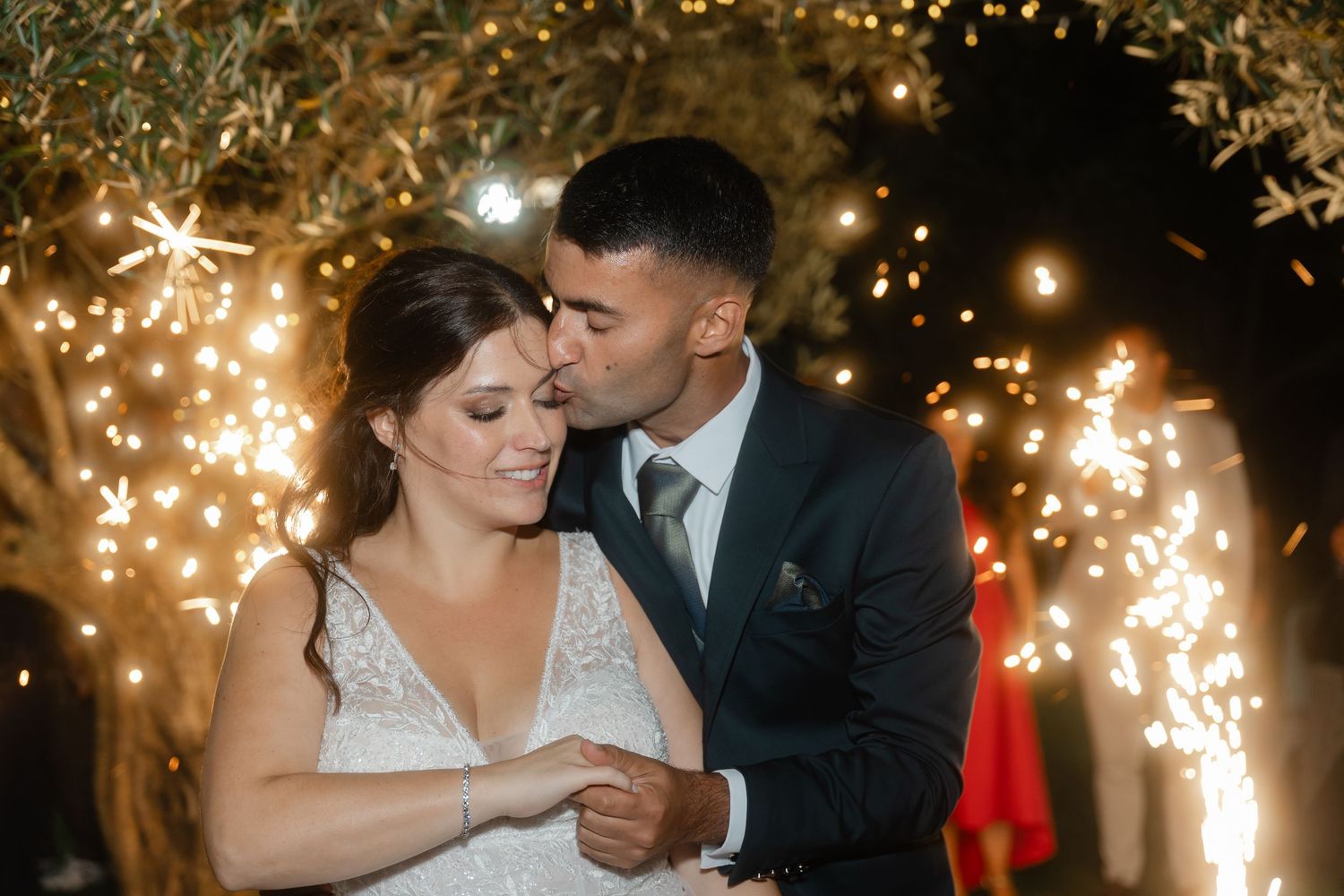A romantic wedding couple dances together under twinkling lights during their first dance at an evening reception.