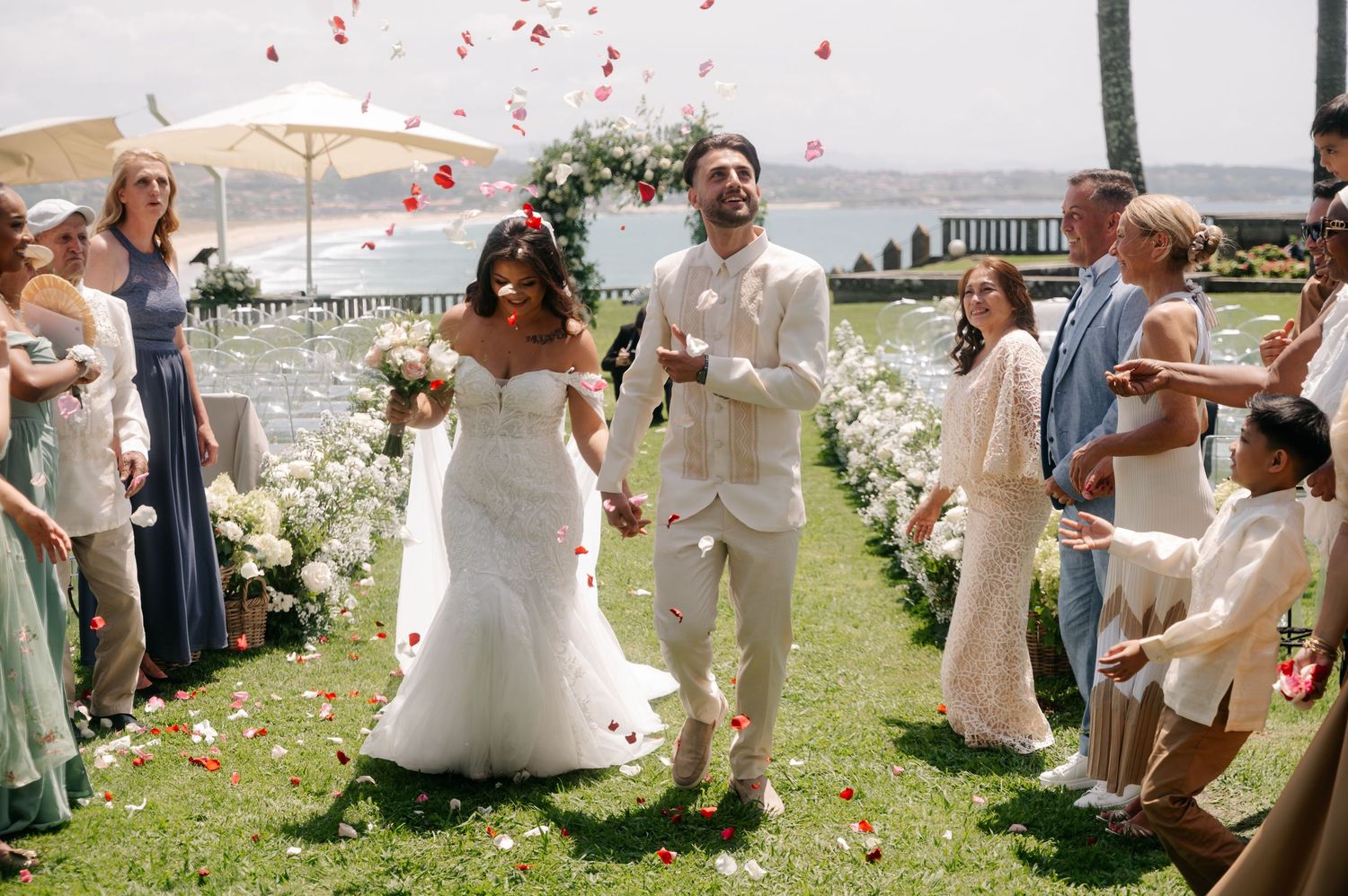 Wedding party celebrates with confetti on a sunny day by the waterfront during outdoor ceremony.