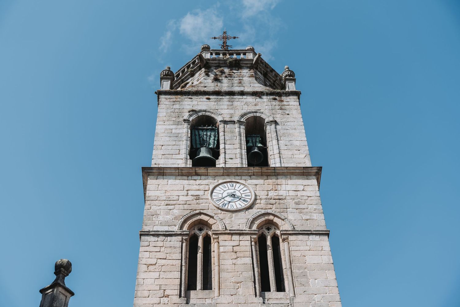 Historic church bell tower with white stone architecture and clock face against blue sky.